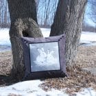 Cushion Two is better, gray velvet cushion with an illustration of two rabbits, outside, leaning against trees.