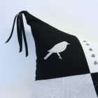 Detail of the pillow Trace of history, corner with embroidered ivory bird on a black background, cushion tip with black ribbons.