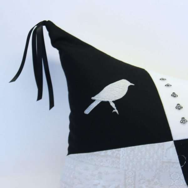 Détail du coussin Trace d'histoire, coin avec oiseau ivoire brodé sur fond noir, pointe du coussin avec rubans noirs.