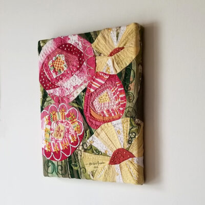 Tableau d'art textile montrant de grosses fleurs de couleurs vives roses et jaunes sur fond vert.
