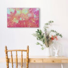 Tableau d'art textile Les jours heureux sur un mur blanc au dessus d'un pupitre avec un bouquet.