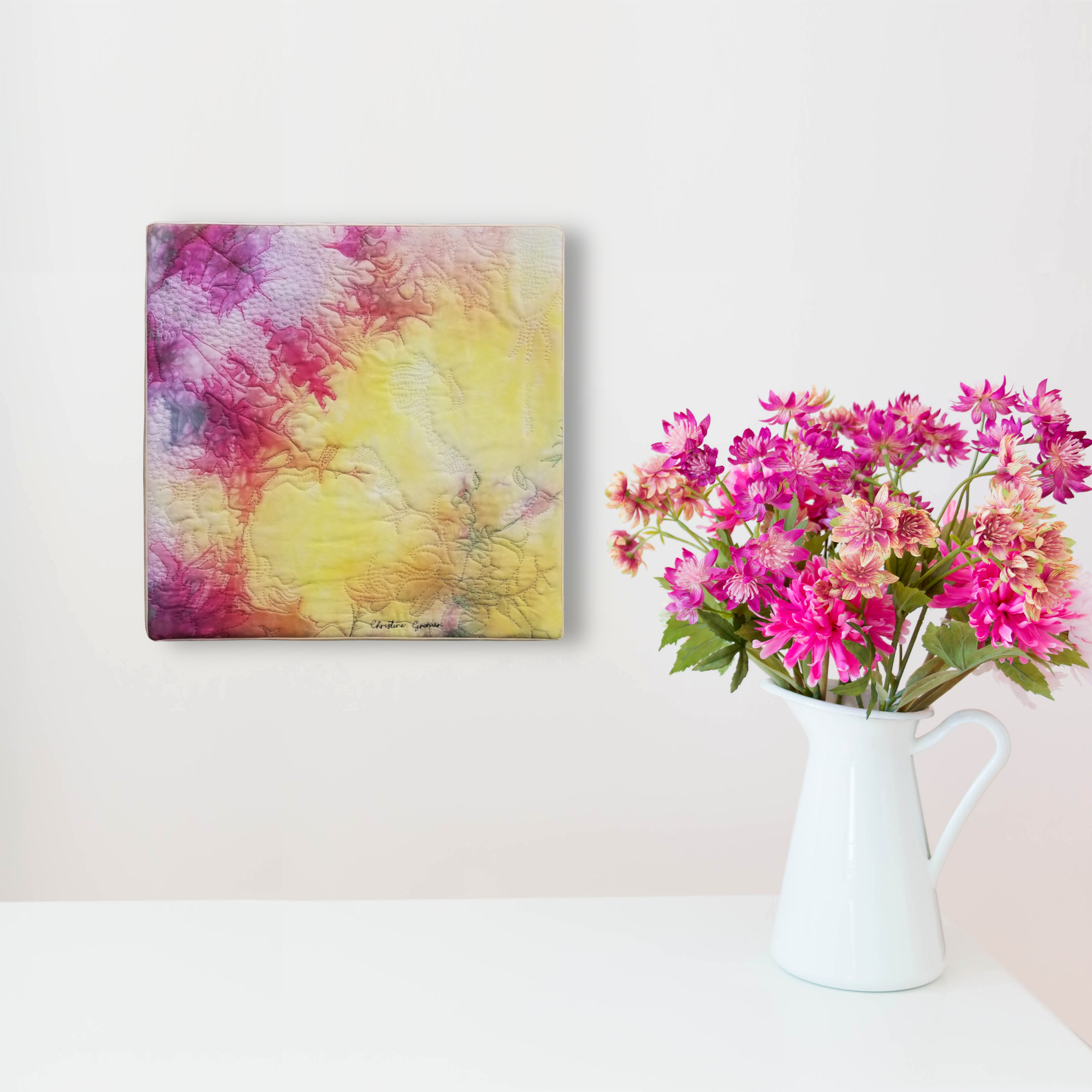 Tableau d'art abstrait rose et jaune sur un mur blanc avec un pichet blanc rempli de fleurs roses.