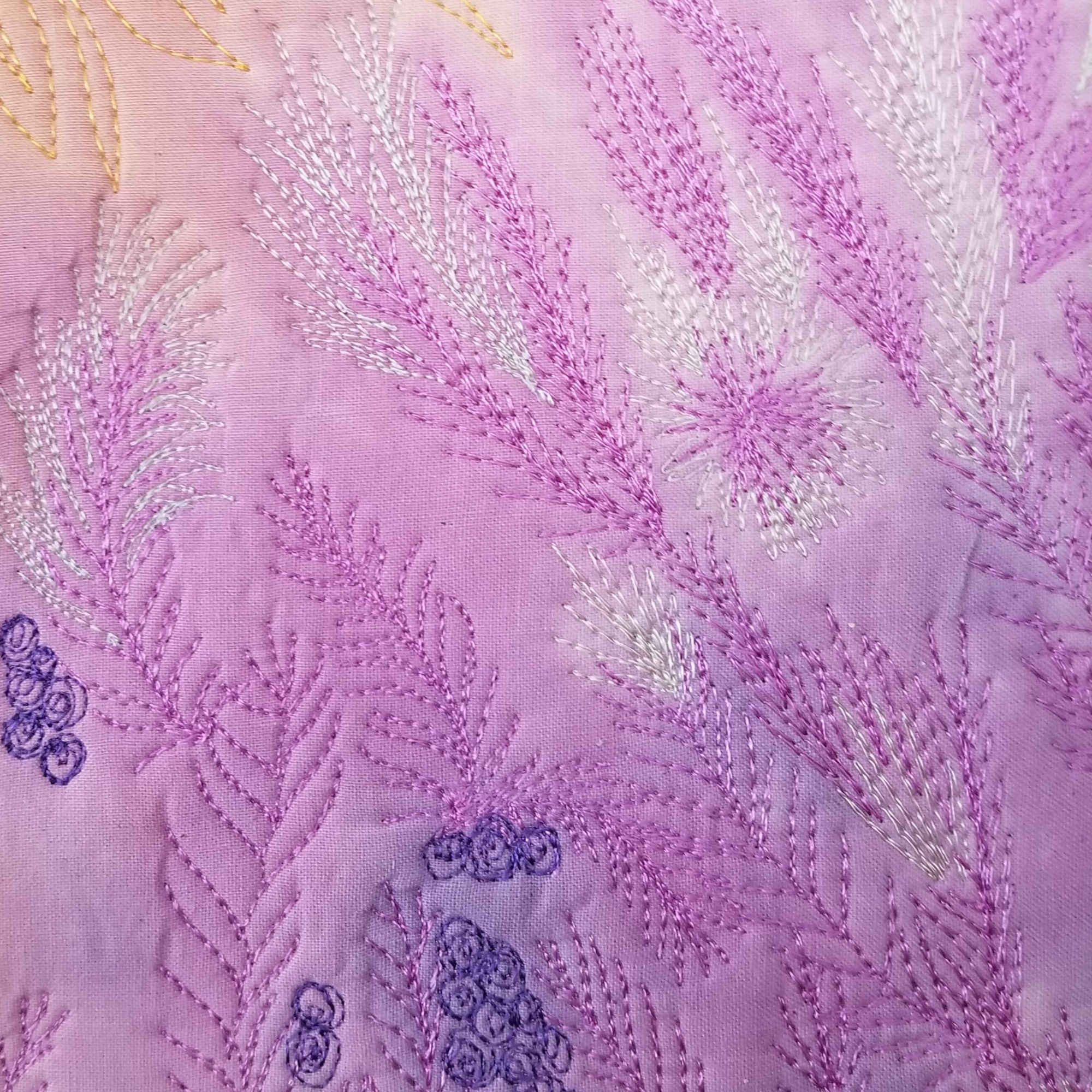 La mémoire du vent – Gros plan sur broderie libre en fil lilas, blanc et bleu sur tissu teint à la main.