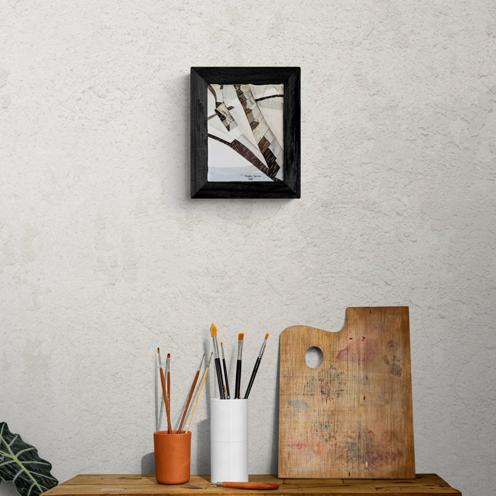 Tableau encadré Matin enneigé sur un mur blanc dans un décor. Le tableau d'art textile figuratif semble abstrait en montrant le détail de branches recouvertes de neige. Couleurs neutres blanc, beige, gris, brun, bleu.