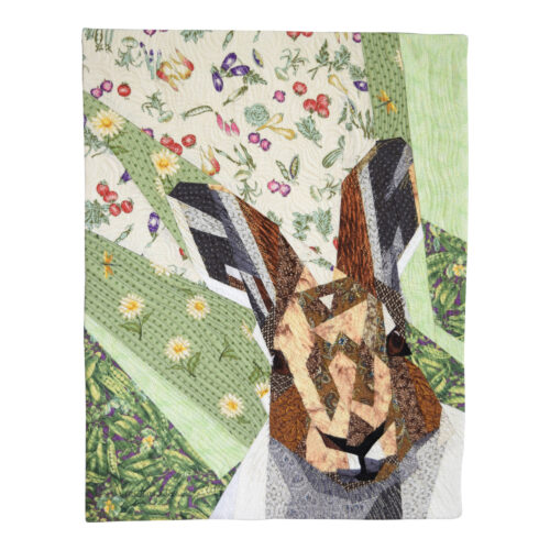 Pièce d'art textile Monsieur Sylvestre. Portrait d'un lièvre espiègle dans le coin droit en diagonale sur un fond de pièces de tissus dans les tons de vert représentant un jardin de légumes.