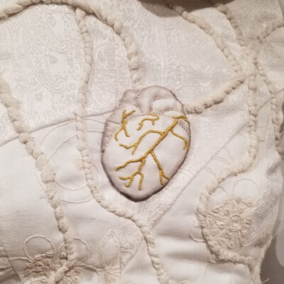 Détail de la sculpture La Vainqueure montrant un coeur brodé de veines ors sur un corsage blanc parcouru de liens comme des racines ou des veines.